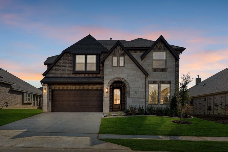 Two-story home with stone and brick exterior, two-car garage, arched entry, and manicured lawn at dusk