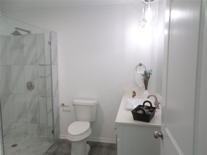 Contemporary bathroom featuring a glass-enclosed shower with large format white and grey-veined tile, a rainfall showerhead, and a built-in shelf