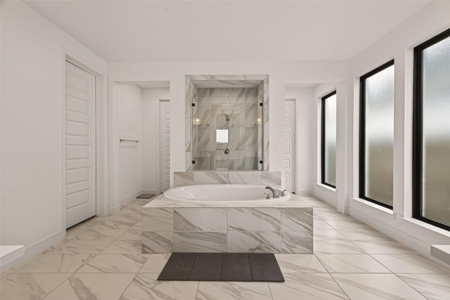 This photo showcases a spacious, modern bathroom featuring a central freestanding bathtub with elegant marble tiling. It includes a glass-enclosed shower, frosted windows for privacy, and a serene, minimalist design.