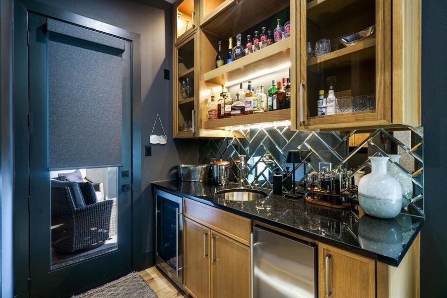 Bar with dark stone countertops, backsplash, ice machine, wine cooler, and sink.  Plus, access to the pool