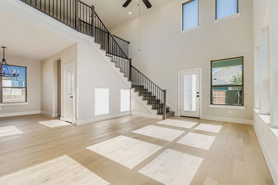 Foyer entrance featuring stairway, a chandelier, light wood-style floors, healthy amount of natural light, and a towering ceiling