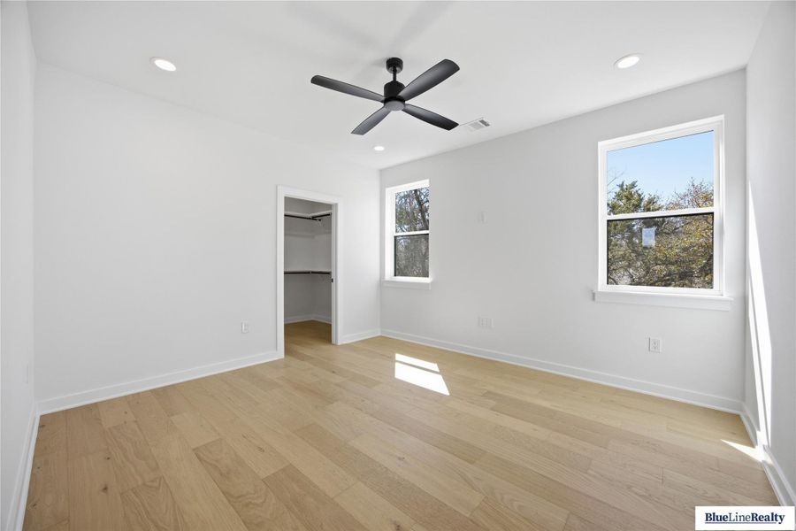 Unfurnished bedroom featuring a walk in closet, light wood-style flooring, a ceiling fan, and recessed lighting
