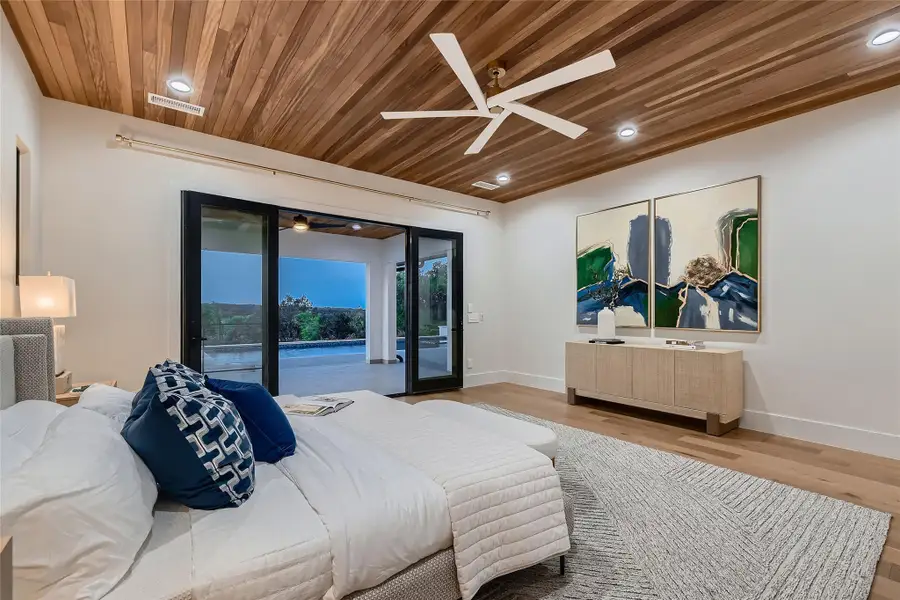 This room features a wood-paneled ceiling with recessed lighting and a ceiling fan, light wood flooring, and access to an outdoor patio with a pool through expansive sliding glass doors