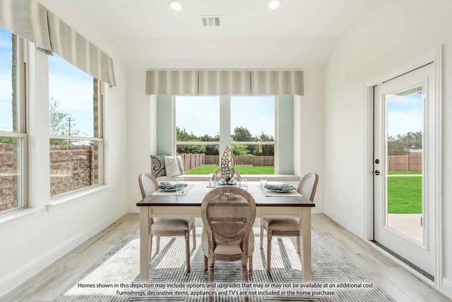 Bright dining area with white table, rattan chairs, large windows, and backyard view through glass door
