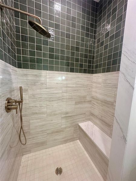A custom tile shower features a built-in bench and modern brass fixtures.