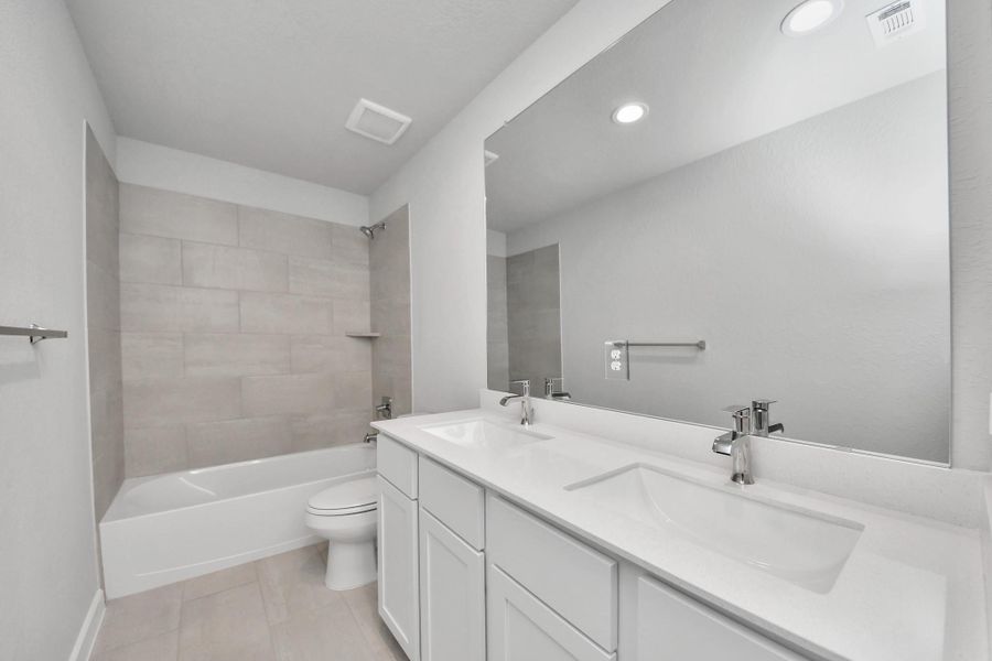 Secondary bath features tile flooring, bath/shower combo with tile surround, light stained wood cabinets, beautiful light countertop. Sample photo of completed home with similar floor plan. Actual colors and selections may vary.