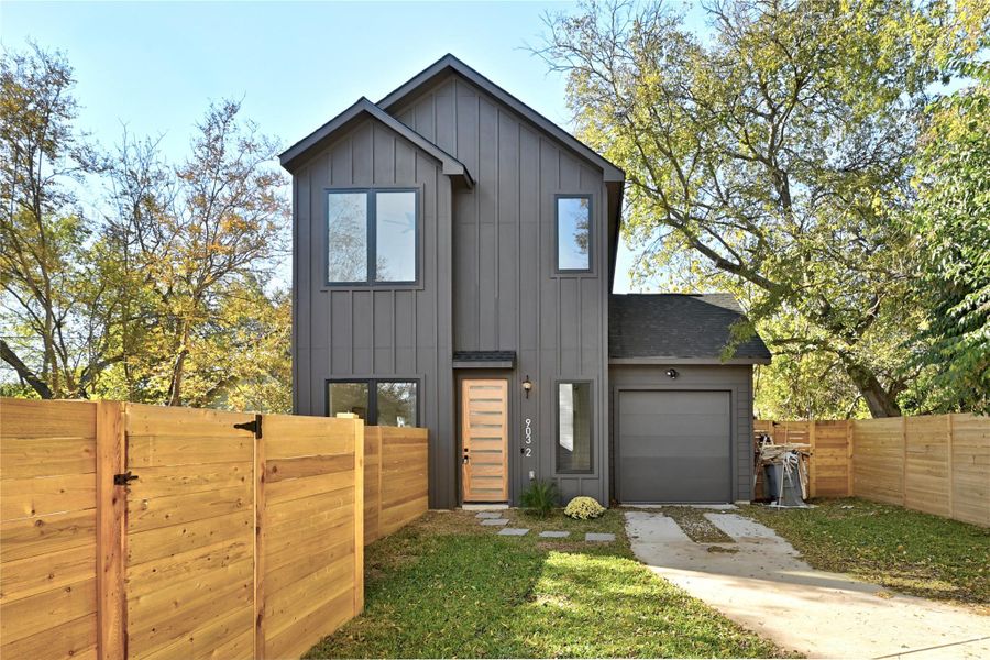 View of front of property with a garage, roof with shingles, board and batten siding, and fence