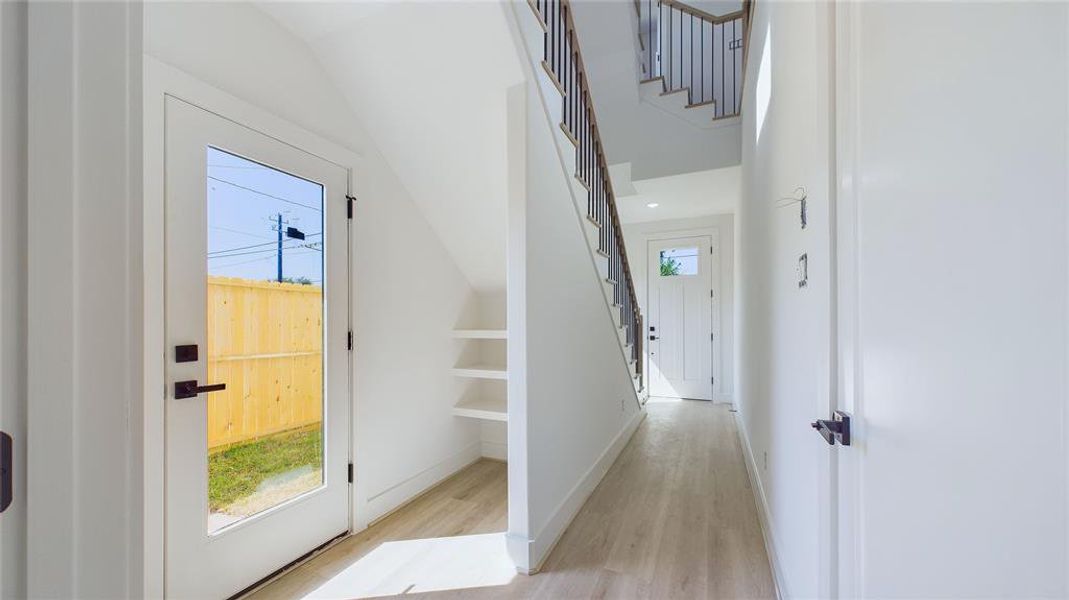 Alternate view of the front entrance showcasing the durable wood-like LVP flooring that extends throughout, ensuring long-lasting quality. Additional shelving under the staircase creates an ideal mudroom, maximizing storage and functionality.