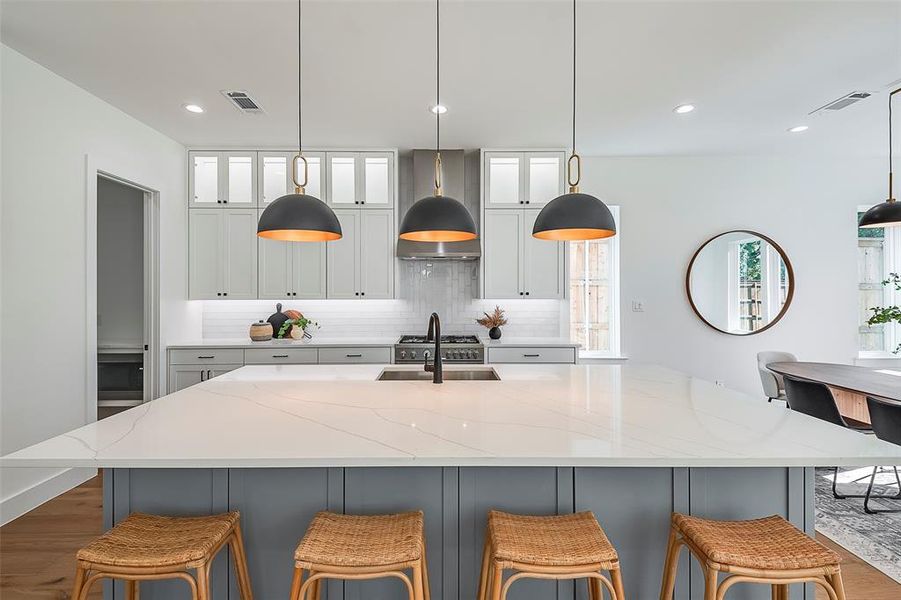 Kitchen with pendant lighting, backsplash, premium range hood, dark wood-type flooring, and light stone countertops