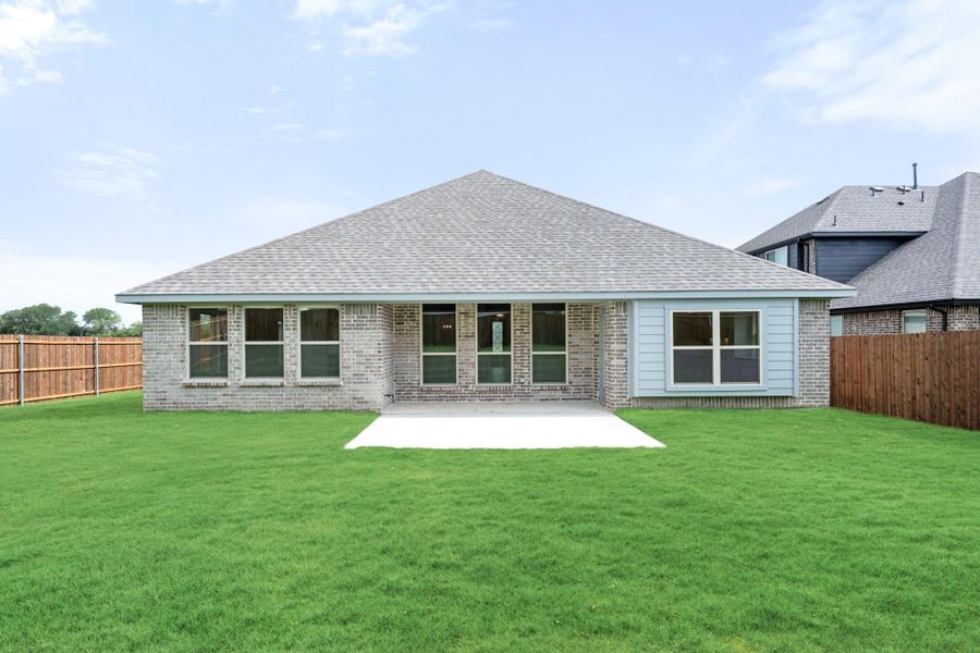 Rear exterior of brick home with covered patio, large fenced backyard, and green lawn