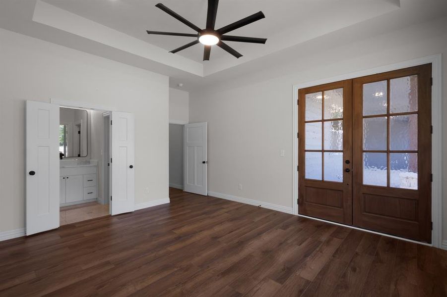 Unfurnished bedroom featuring baseboards, a raised ceiling, dark wood-style flooring, ensuite bath, and french doors