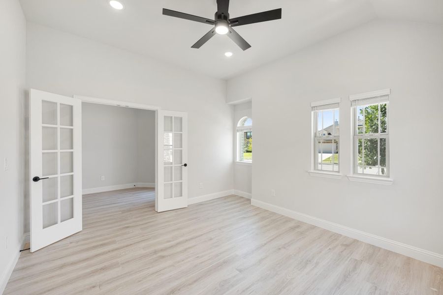 Empty room with light wood floors, French doors, black ceiling fan, and two windows