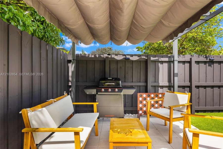 Outdoor living space featuring a retractable fabric canopy, paved patio, dark wood-finish privacy fencing, and a built-in outdoor gas grill