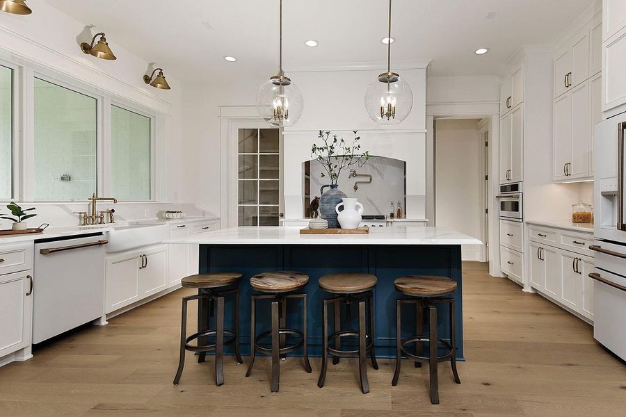Stunning kitchen has large central island with room for seating in a striking custom accent color. Elegant pendant lights are the perfect jewelry.