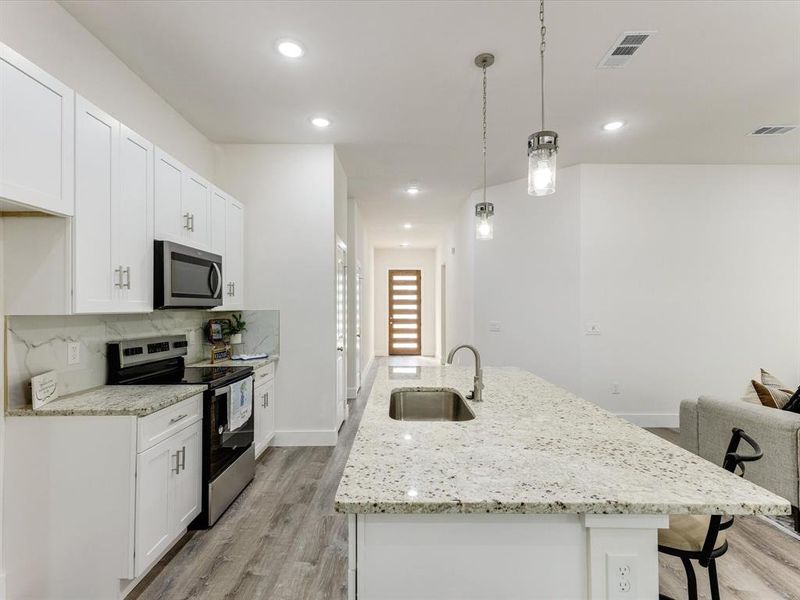 Kitchen with stainless steel appliances, an island with sink, white cabinetry, a kitchen breakfast bar, and light stone countertops