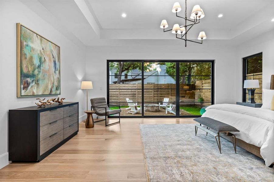 Bedroom with access to exterior, light hardwood flooring, an luxury lighting, and a tray ceiling