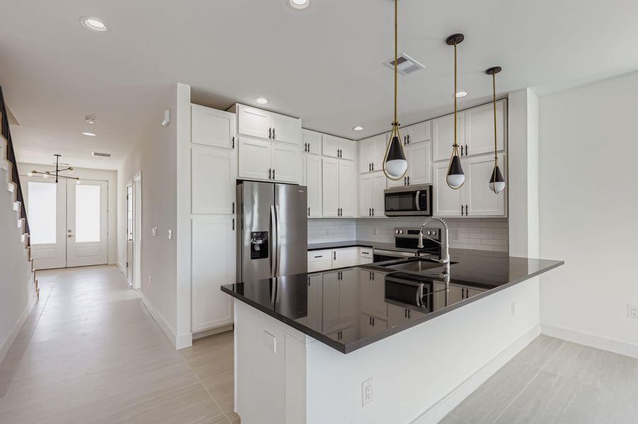 Kitchen with appliances with stainless steel finishes, hanging light fixtures, decorative backsplash, white cabinets, and a peninsula