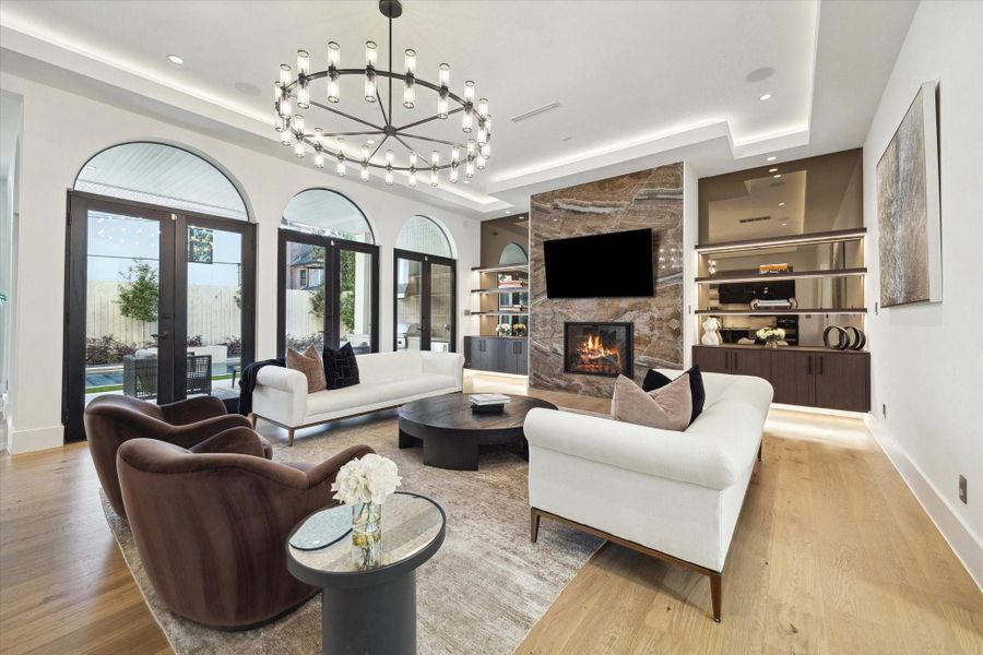 A beautiful living room is the heart of every home. Alternate view showcasing the custom-built glass shelves, porcelain wall surrounding the fire place and multiple doors revealing the covered outdoor patio and pool
