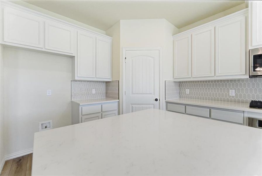 Kitchen with decorative backsplash, light stone counters, and white cabinetry