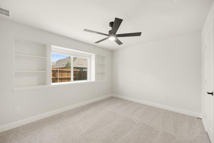 Empty bedroom with carpet, ceiling fan, and built-in shelves flanking a window