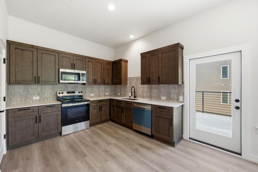 Kitchen featuring appliances with stainless steel finishes, dark brown cabinetry, decorative backsplash, light wood finished floors, and recessed lighting