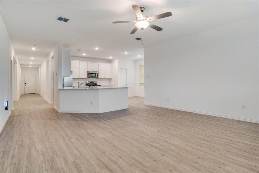 Kitchen with open floor plan, white cabinetry, a ceiling fan, light wood-style flooring, and stainless steel appliances