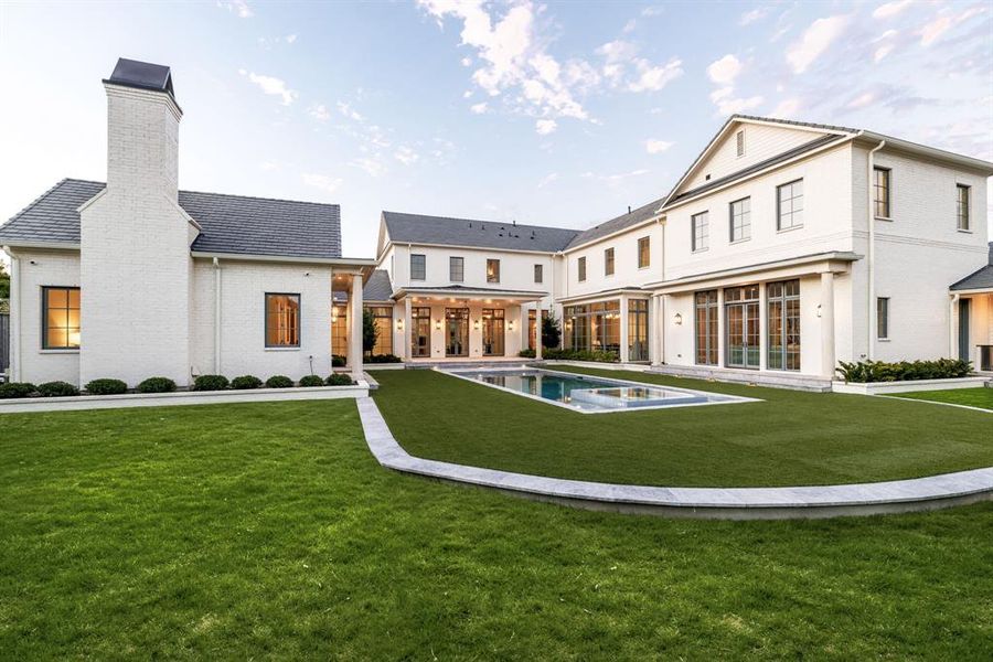 Back of property with a patio, a chimney, brick siding, a pool with connected hot tub, and a lawn Back of property with a patio, a chimney, brick siding, a pool with connected hot tub, and a lawn