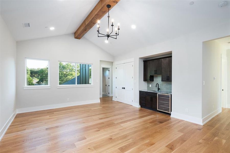 Unfurnished living room featuring sink, beamed ceiling, light wood-type flooring, high vaulted ceiling, and beverage cooler