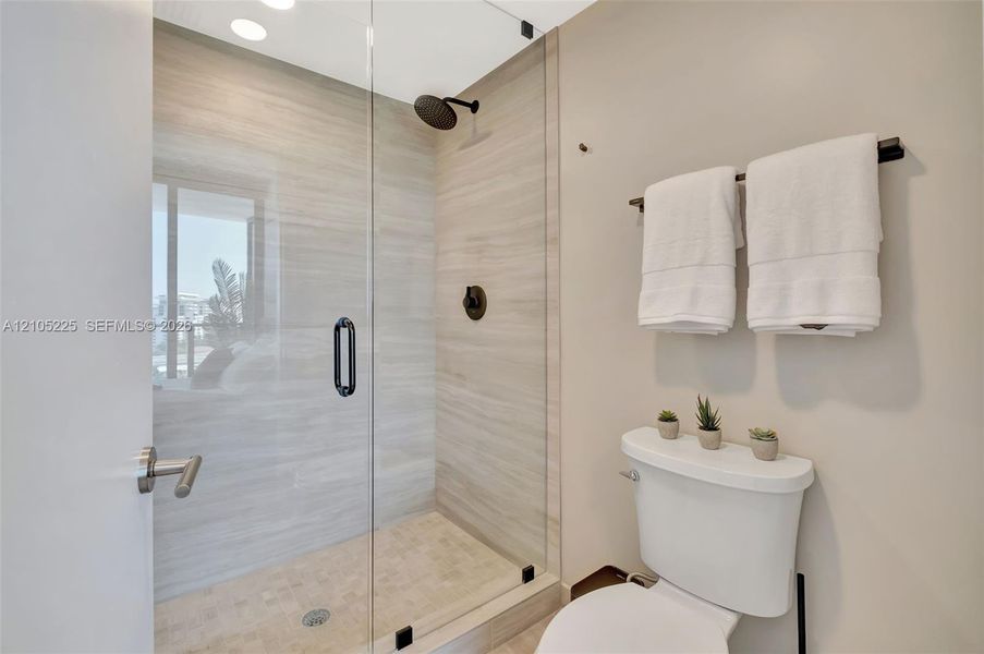 Walk-in shower featuring a frameless glass enclosure, horizontal stone-finish tile surround, textured stone-finish floor tile, and matte black plumbing fixtures