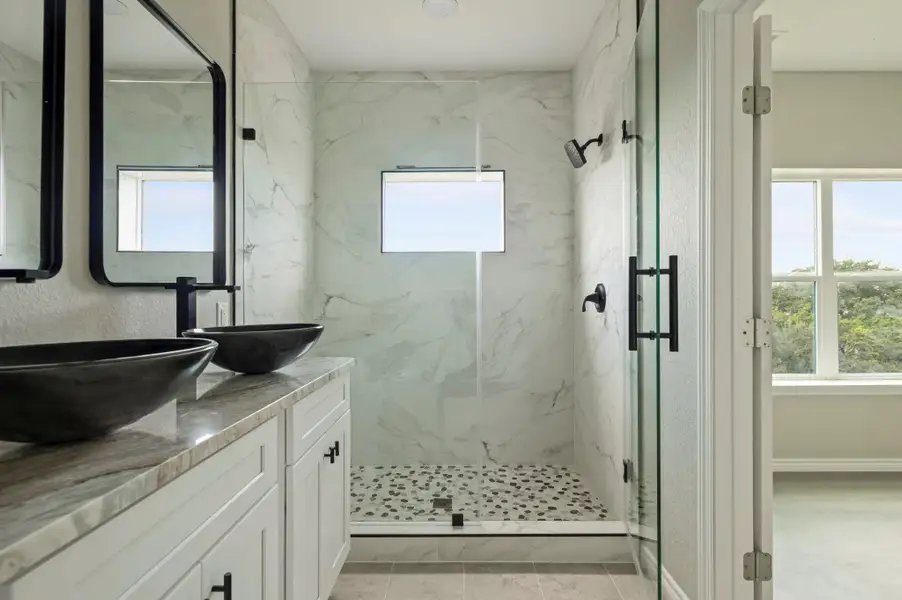 Full bath with a marble finish shower, double vanity, a textured wall, and light tile patterned floors