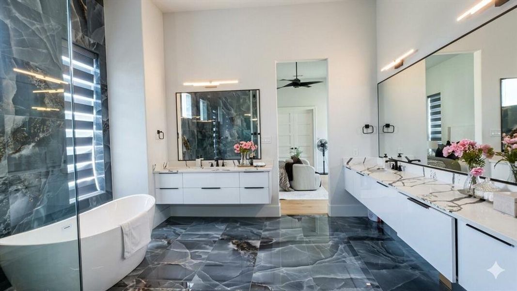 Spacious bathroom featuring large-format dark stone flooring, a freestanding soaking tub, and a shower with a floor-to-ceiling glass enclosure