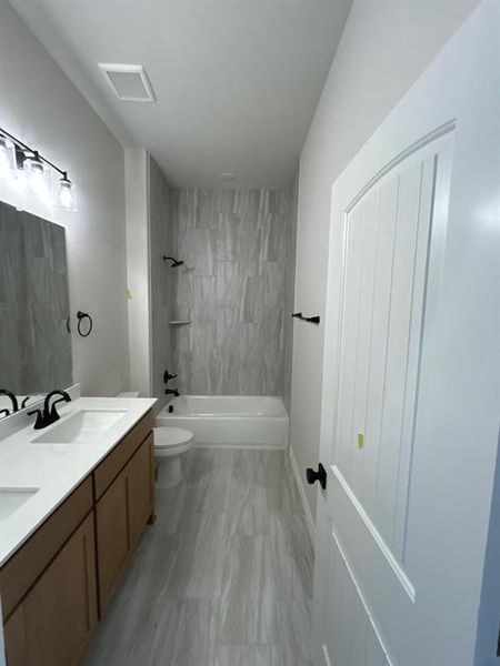 Bathroom featuring a dual vanity with white countertops, a tub/shower combination with tile surround, wood-finish flooring, and matte black fixtures