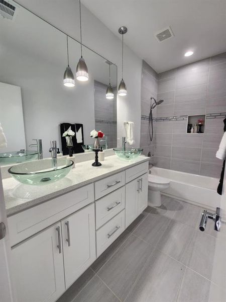 Full bathroom featuring double vanity, tile patterned flooring, toilet, and tiled shower / bath