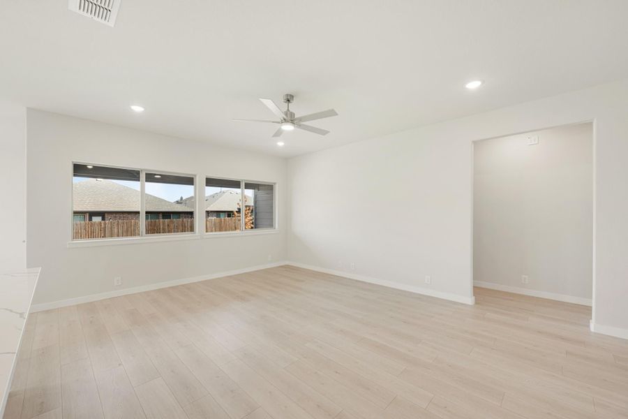 Empty living room with light wood floors, ceiling fan, and large windows