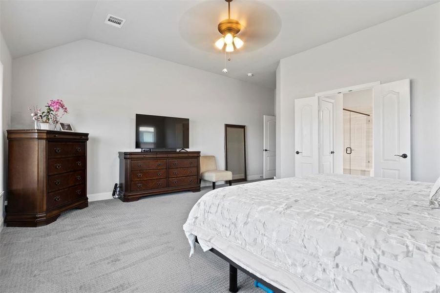 Carpeted bedroom with ceiling fan, vaulted ceiling, and ensuite bath