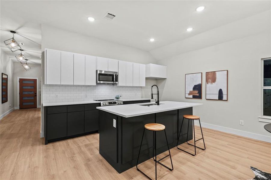 Kitchen with appliances with stainless steel finishes, a kitchen island with sink, sink, light hardwood / wood-style floors, and white cabinetry