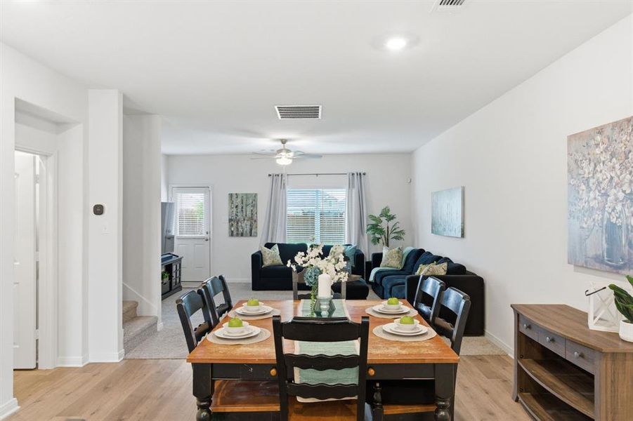 An inviting open-concept living space featuring light-toned flooring, a dining area with a wooden table, and a living area with a ceiling fan