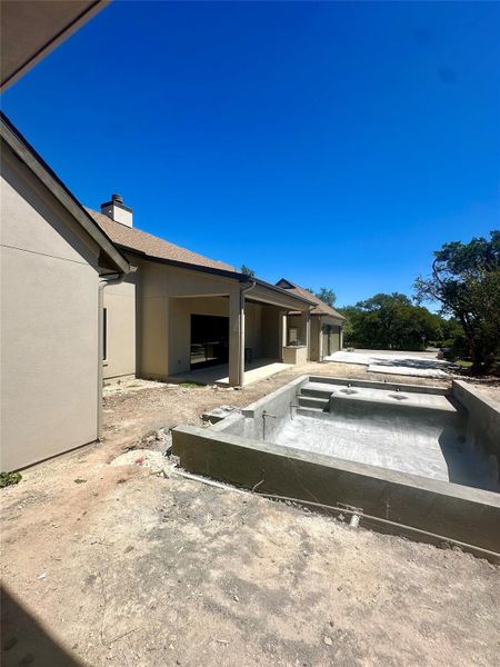 An in-progress pool shell sits adjacent to the covered back porch of this modern home.