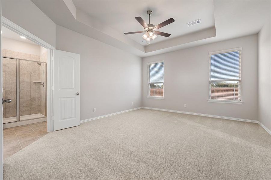 Unfurnished bedroom with a tray ceiling, ceiling fan, light colored carpet, light tile patterned floors, and ensuite bath Unfurnished bedroom with a tray ceiling, ceiling fan, light colored carpet, light tile patterned floors, and ensuite bath