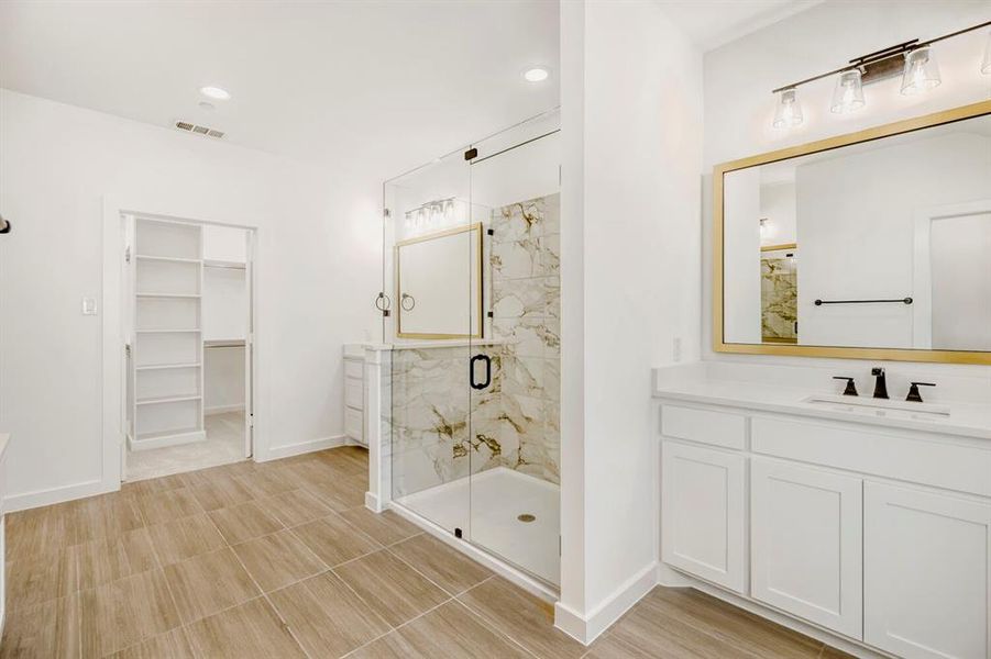 White bathroom featuring wood-finish tile flooring, a glass-enclosed shower with marble-look wall tile, and a white vanity with a quartz countertop