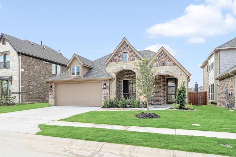 Single-story home with brick and stone exterior, arched entry, two-car garage, and manicured front lawn