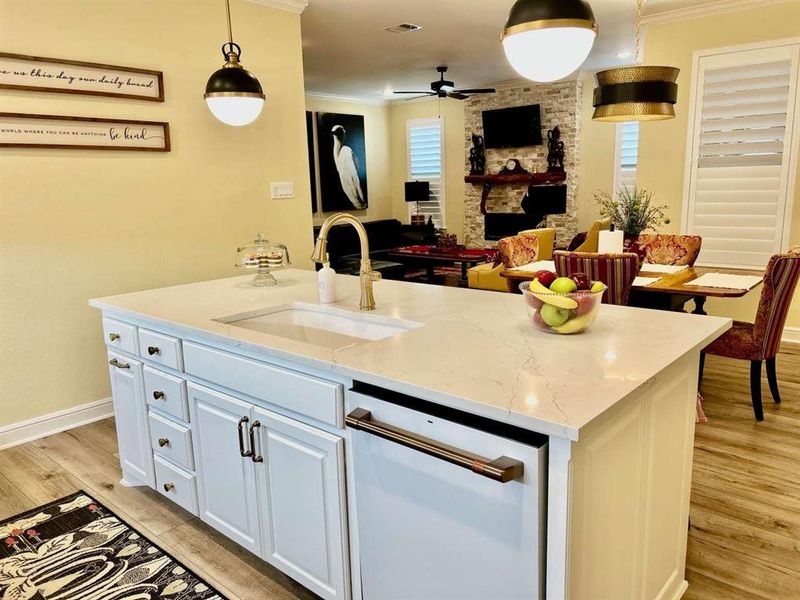 Kitchen with sink, white cabinetry, hanging light fixtures, a center island with sink, and light stone countertops