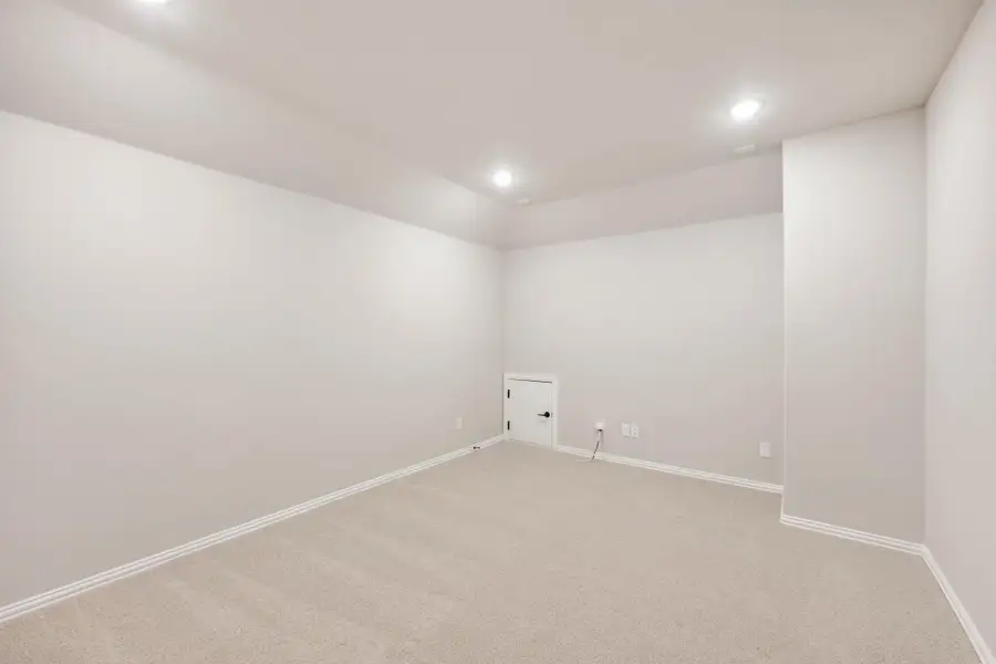 Empty basement room with beige carpet, white walls, recessed lighting, and a small utility door. Empty basement room with beige carpet, white walls, recessed lighting, and a small utility door.
