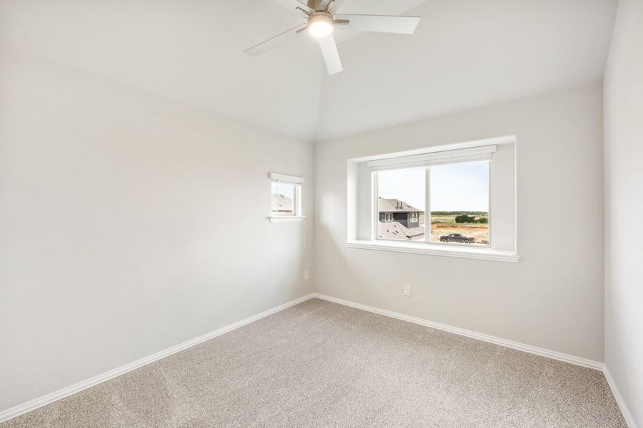 Empty bedroom with carpet flooring, ceiling fan, vaulted ceiling, and two windows with neighborhood view