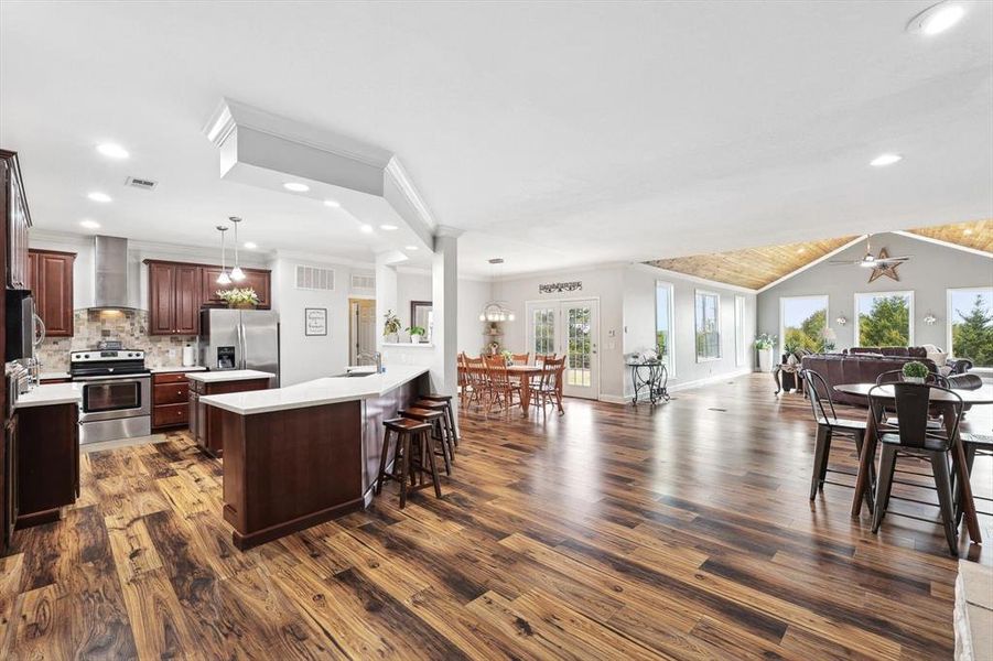 Kitchen featuring appliances with stainless steel finishes, backsplash, dark hardwood / wood-style flooring, hanging light fixtures, and wall chimney range hood