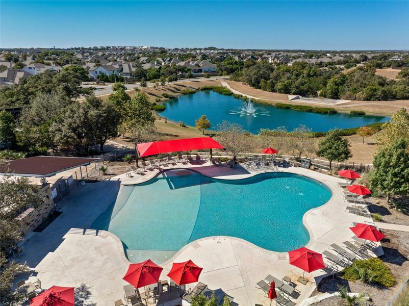 This property features a large outdoor swimming pool with a surrounding paved deck, several lounge chairs, and red umbrellas