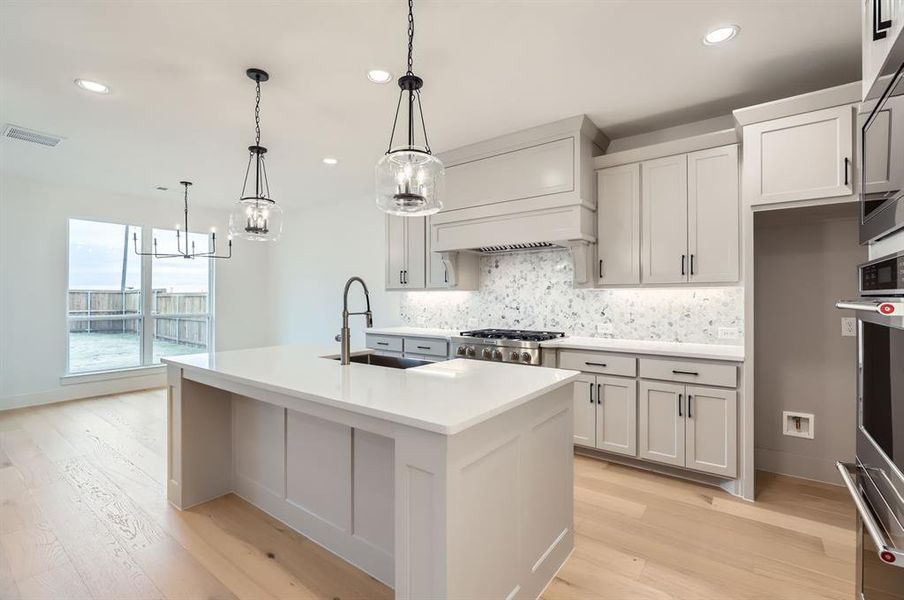 Kitchen with appliances with stainless steel finishes, light wood-type flooring, sink, pendant lighting, and a center island with sink