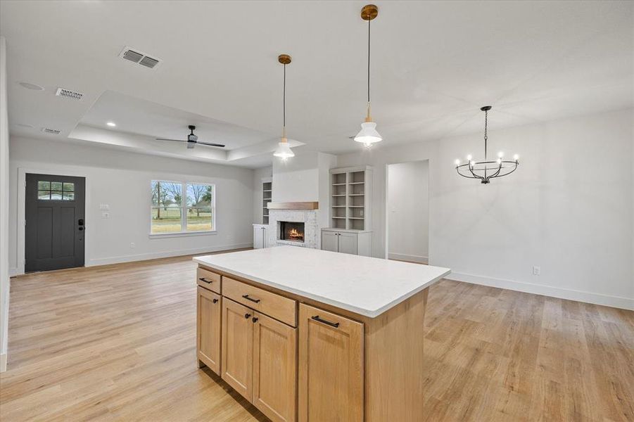 Kitchen featuring light brown cabinetry, a center island, hanging light fixtures, light wood-type flooring, and a tray ceiling