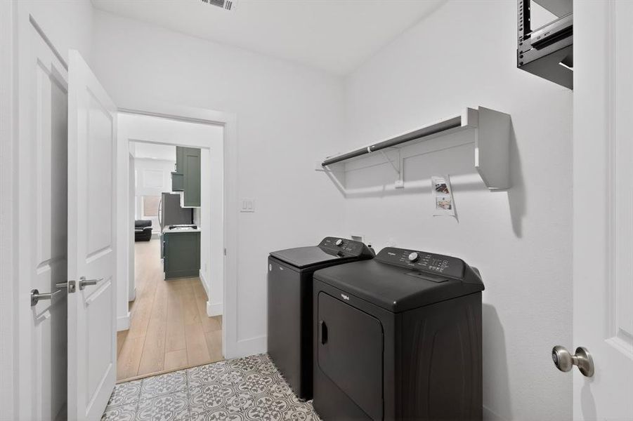 Dedicated laundry area featuring patterned floor tile, overhead shelving, and light wood-finish flooring visible beyond the doorway Dedicated laundry area featuring patterned floor tile, overhead shelving, and light wood-finish flooring visible beyond the doorway