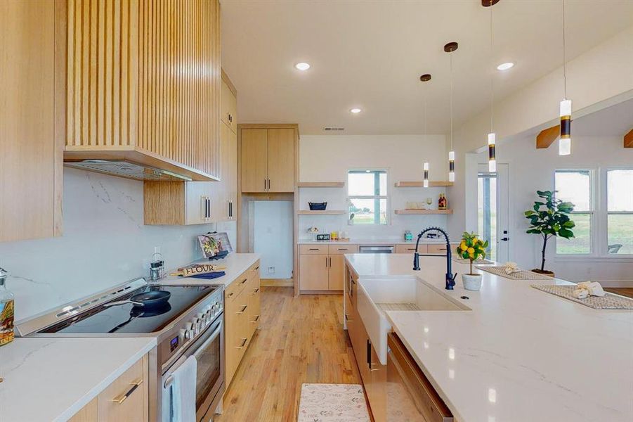 Kitchen featuring light hardwood / wood-style flooring, stainless steel range oven, light brown cabinetry, light stone counters, and hanging light fixtures